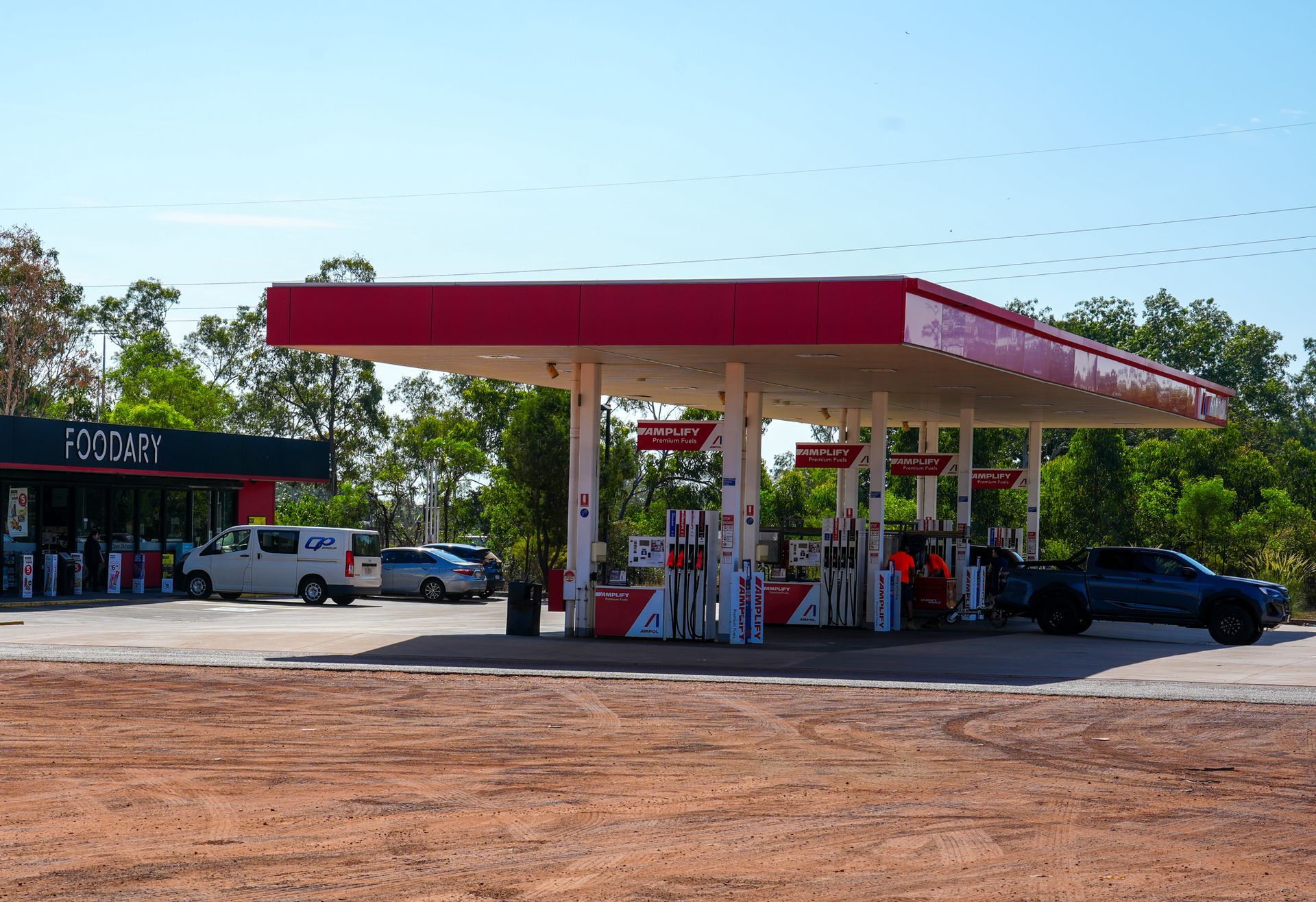 Gas station with red and white canopy; vehicles parked at pumps and a store building.