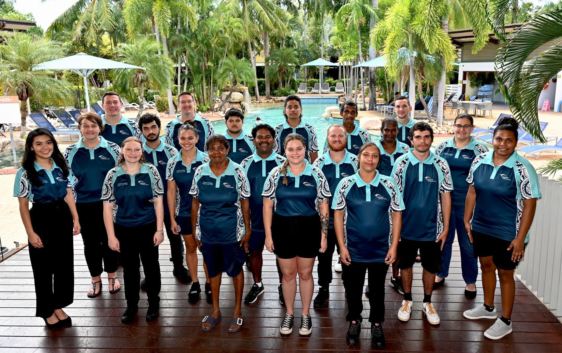 Group of people in teal polo shirts posing near a pool.