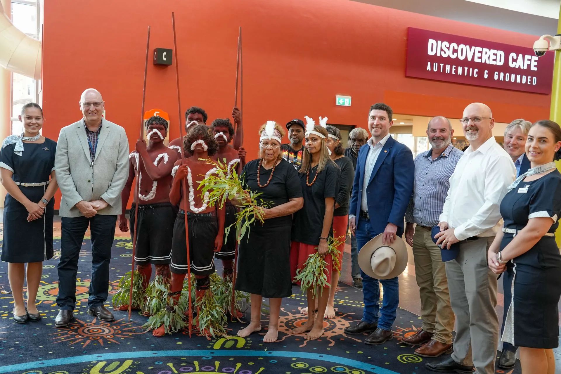 Group of people, including Indigenous Australians in traditional attire, at the opening of a cafe.