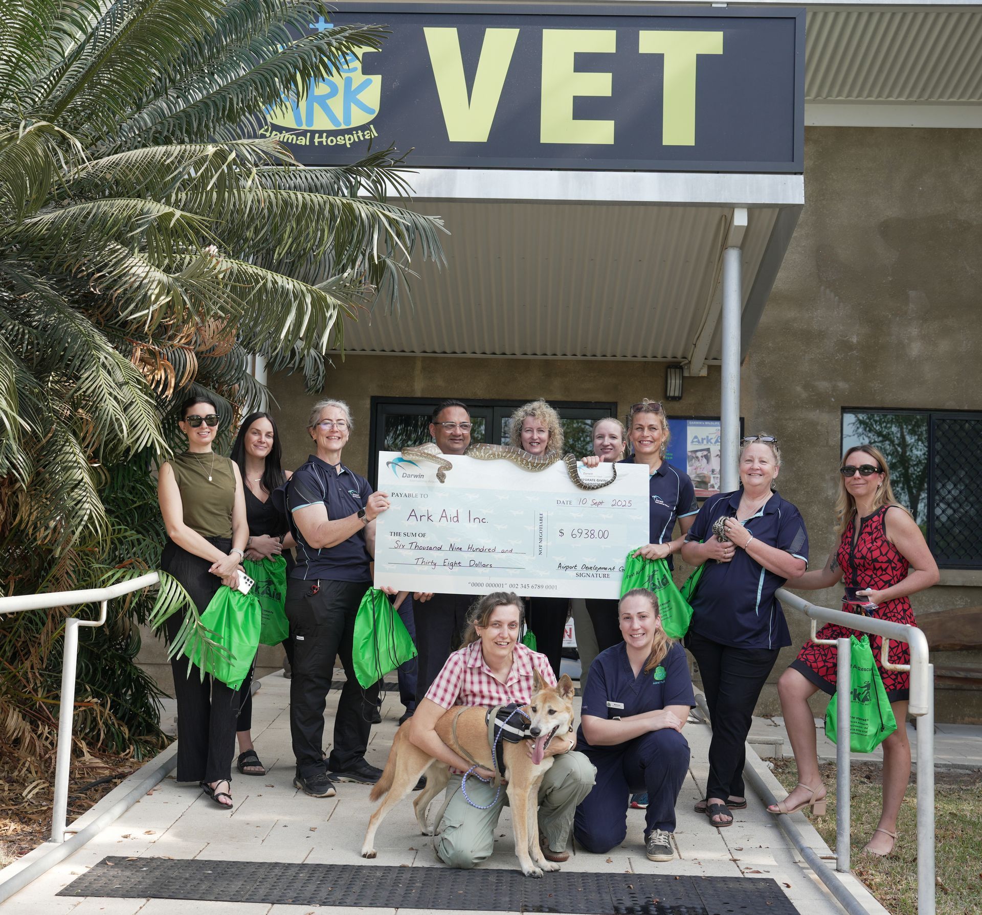 Group of people holding a large check outside a vet clinic, posing with a dog.