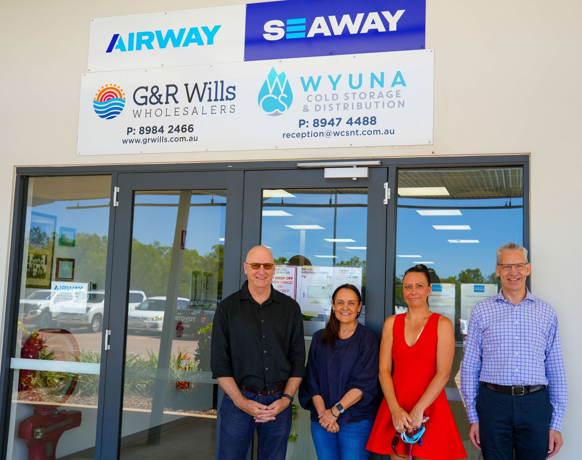 Four people standing outside a storefront with Airway, Seaway, G&R Willis, and Wyna signs above the entrance
