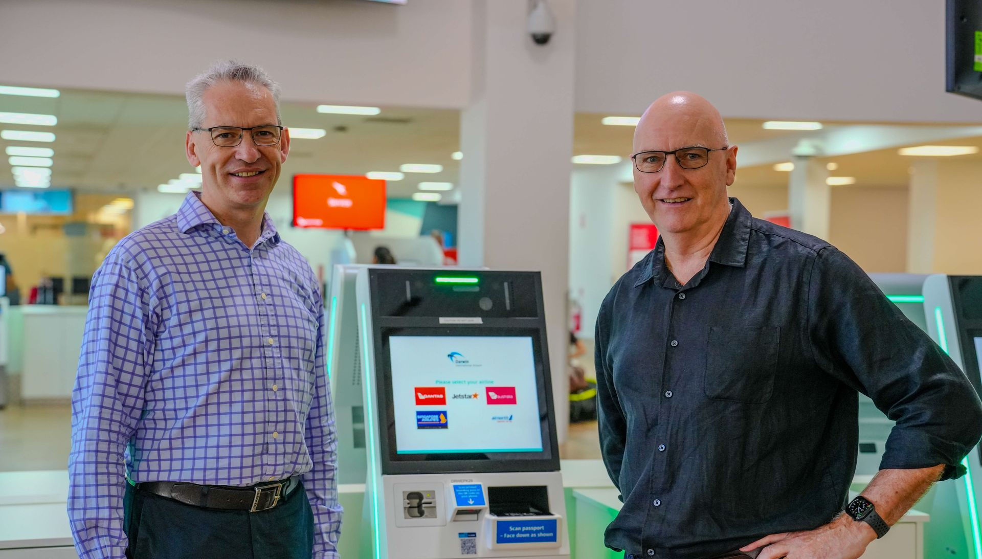 Two men standing beside a touchscreen kiosk in a bright office lobby