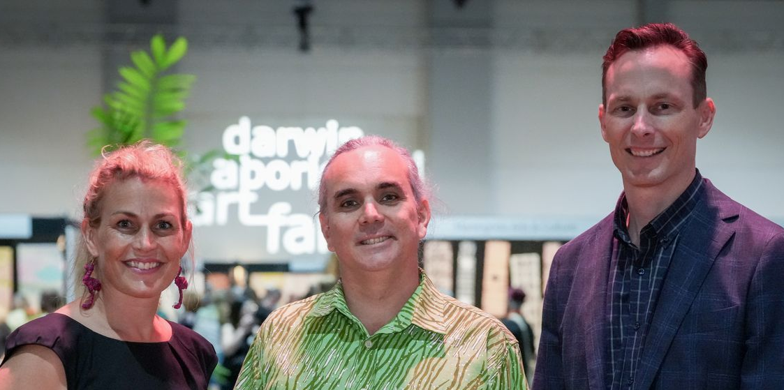 Three people smiling at a Darwin Aboriginal Art Fair event.