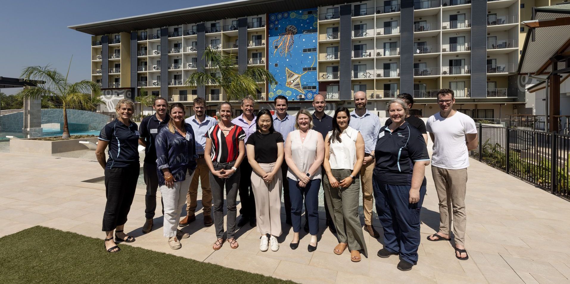 Group of people standing in front of a building. Bright blue sky, sunny day.