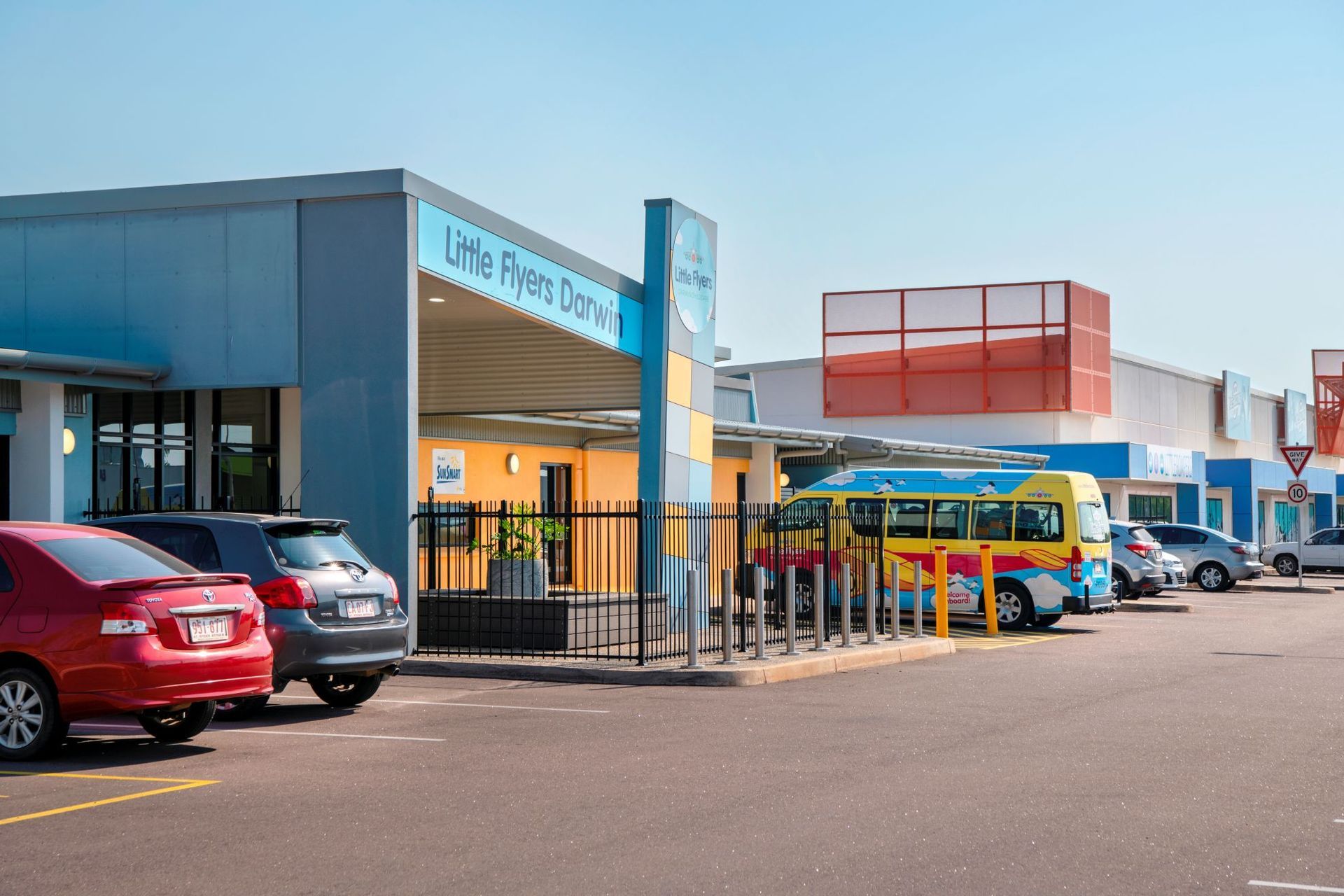 Daycare building with cars in parking lot; a colorful school bus is parked out front.