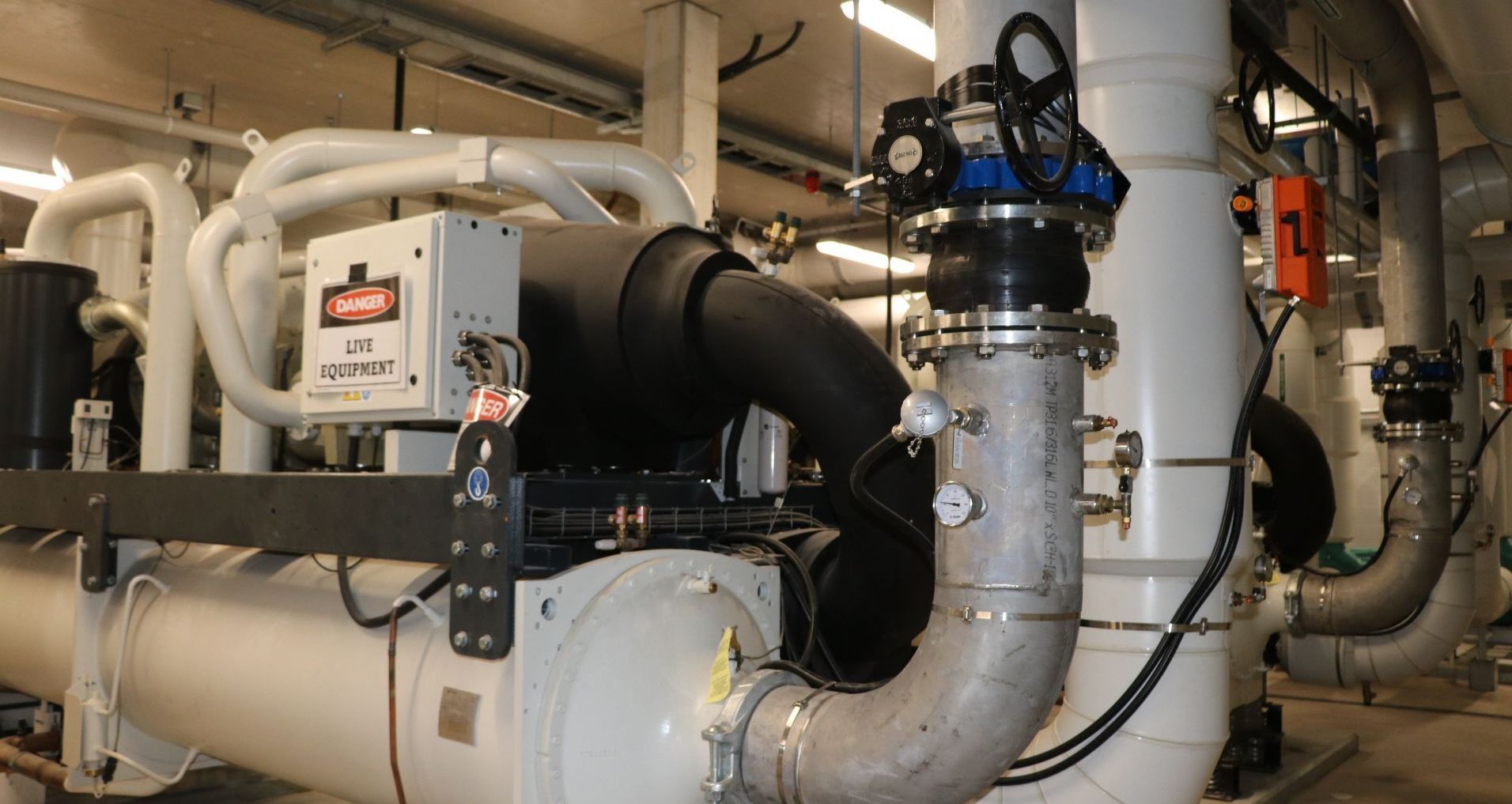 Mechanical room with large chiller, pipes, and control panel.