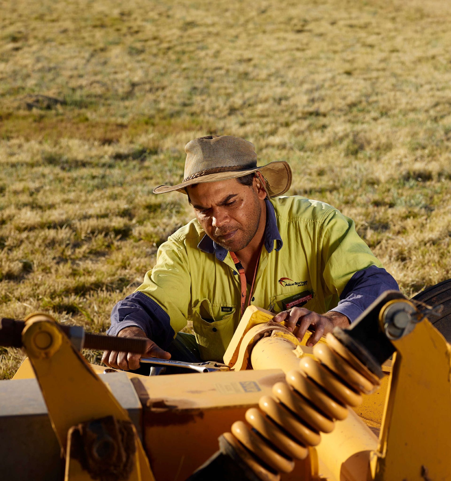 A man in a green shirt is working on a yellow machine