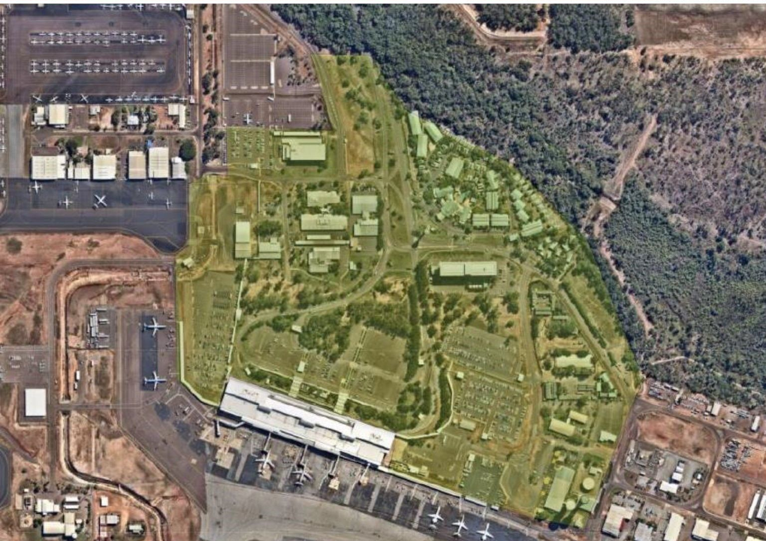 Aerial view of an airport complex with buildings, parking, and runways, highlighted in yellow, next to a forest.
