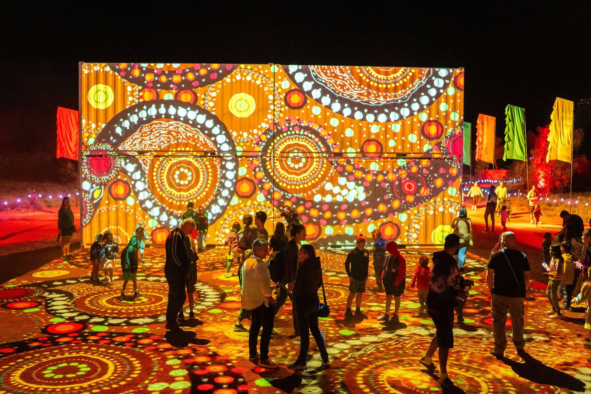 A group of people are standing in front of a large screen at night.