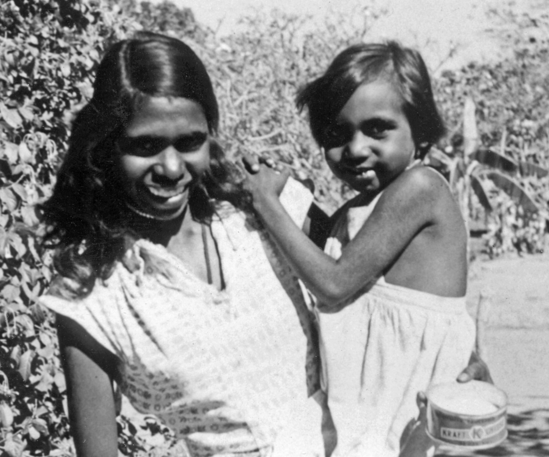 Woman and child outdoors. Woman smiles, child rests arm on her shoulder and holds a bowl.
