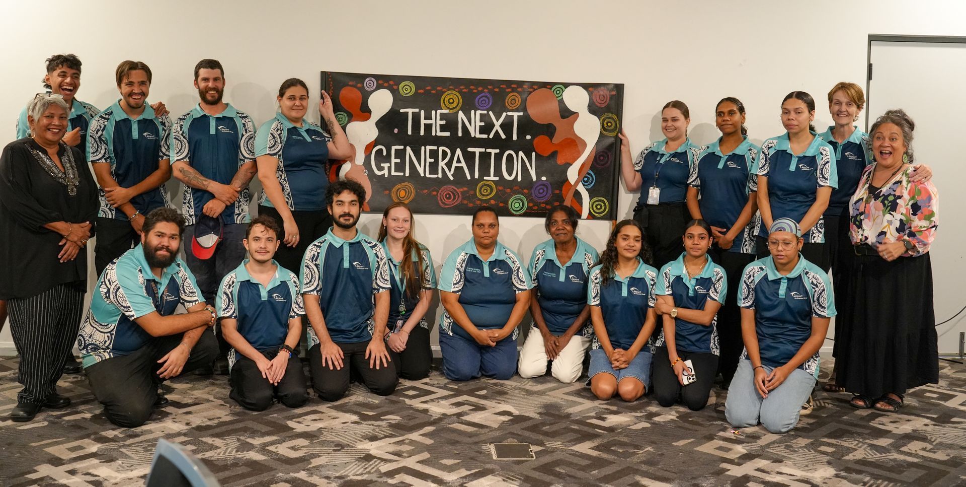 Group of people, possibly Indigenous, in blue shirts, posing for a photo in front of a 