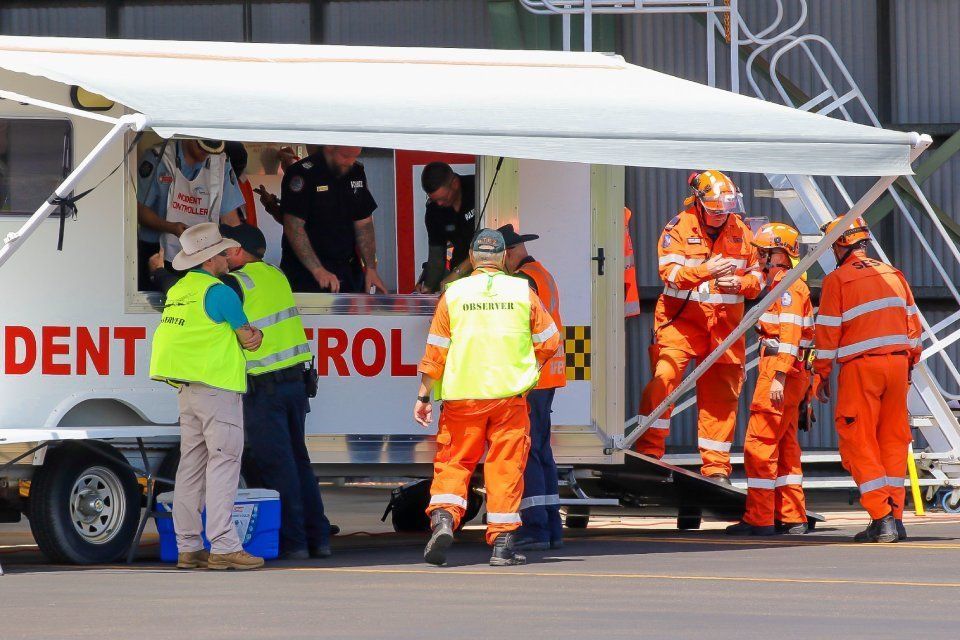 Emergency responders in orange suits near a mobile Incident Control unit at an airport.