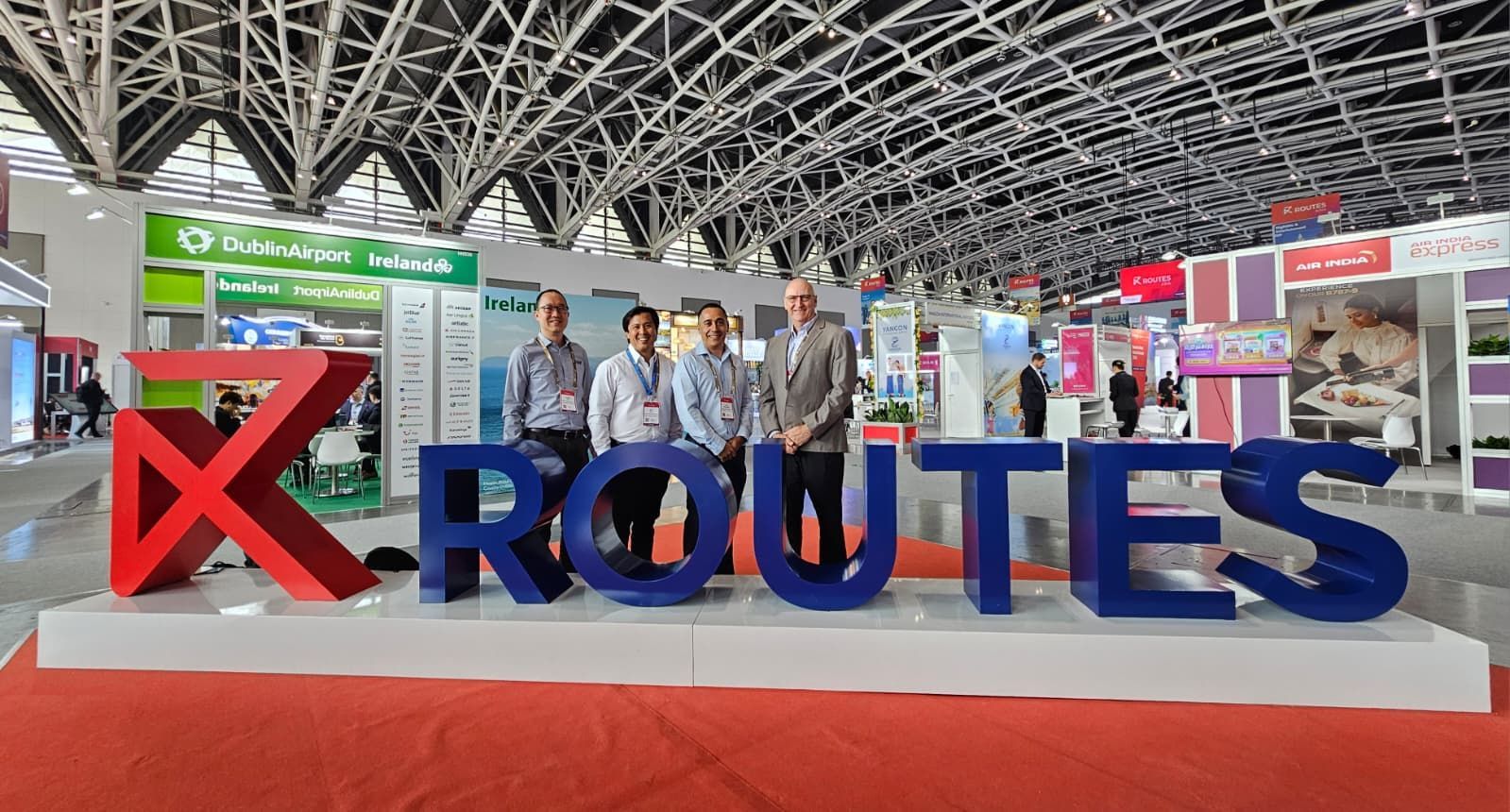 RXROUTES booth at an expo, with large blue and red letters and several people standing behind it