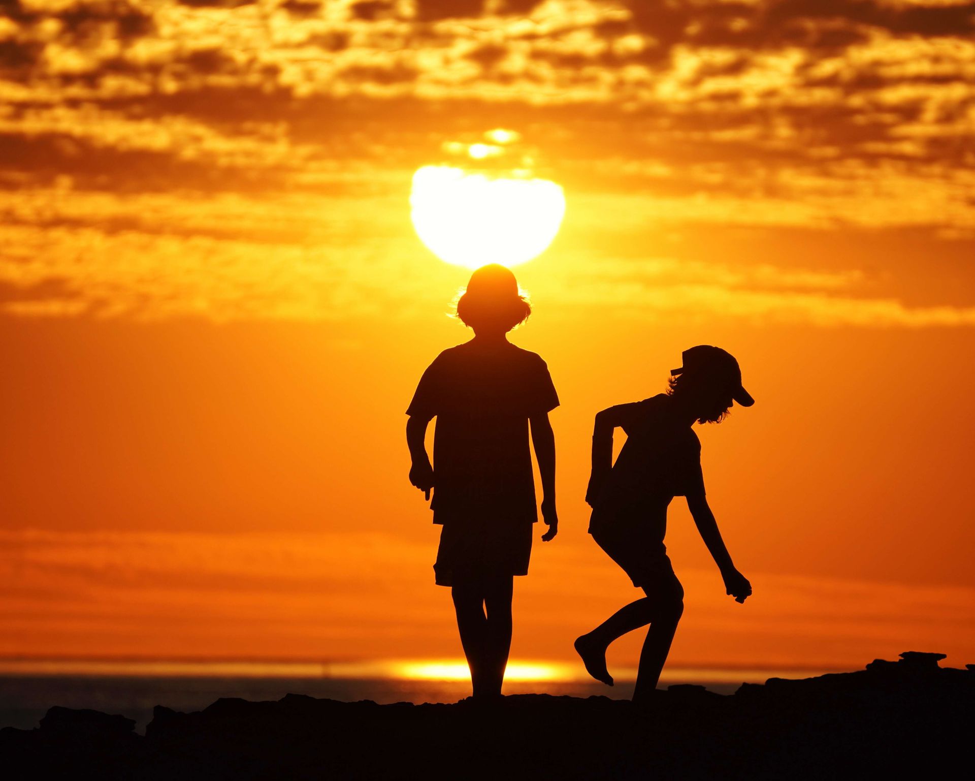 A boy and a girl are standing in front of the sun at sunset