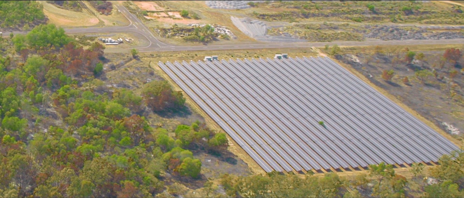 Aerial view of a solar panel farm in a rural landscape. Rows of panels take up most of the frame.