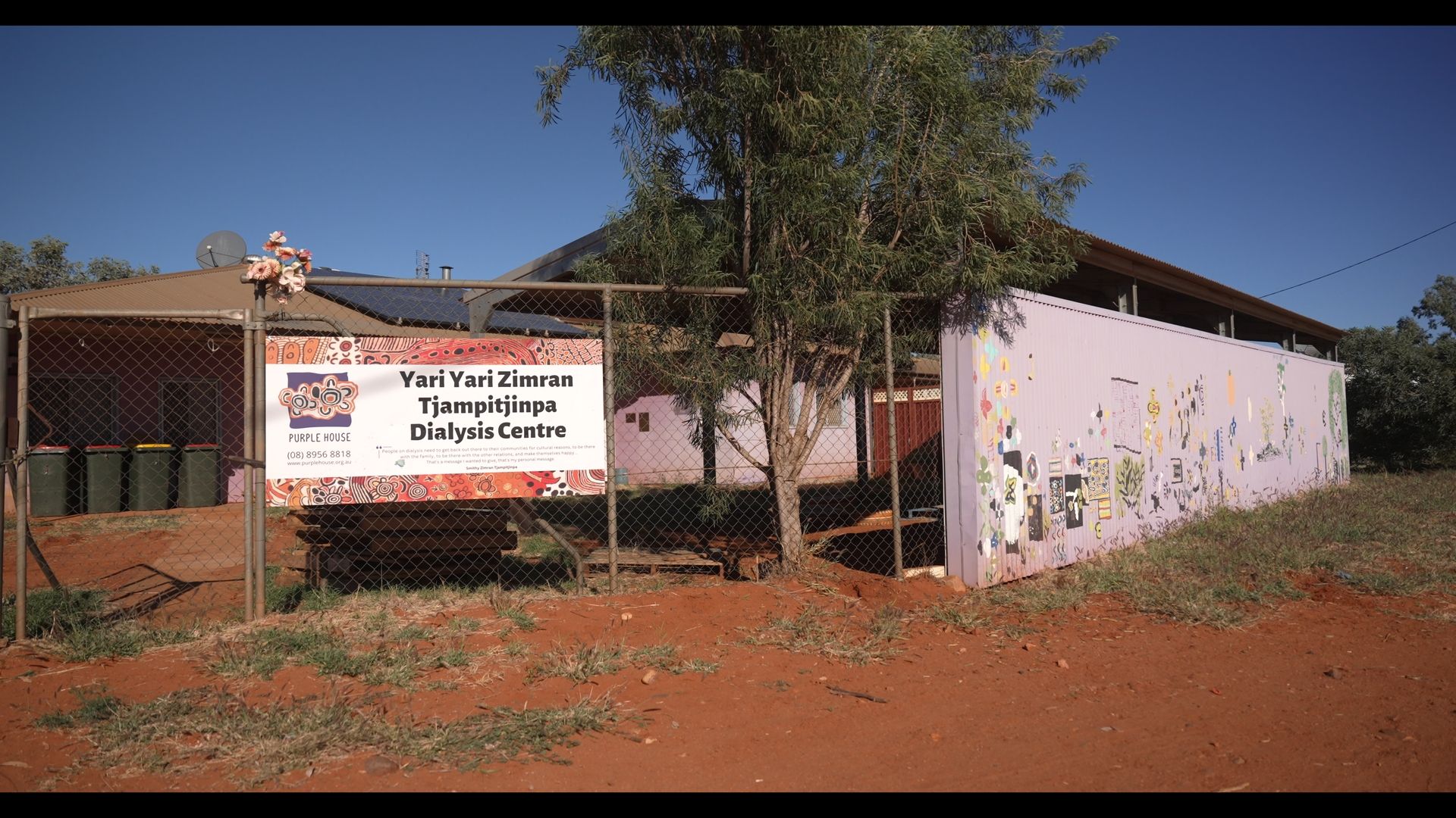 Yard Yila Art Centre in Australia, sign, fence, and building on red dirt under a clear blue sky.