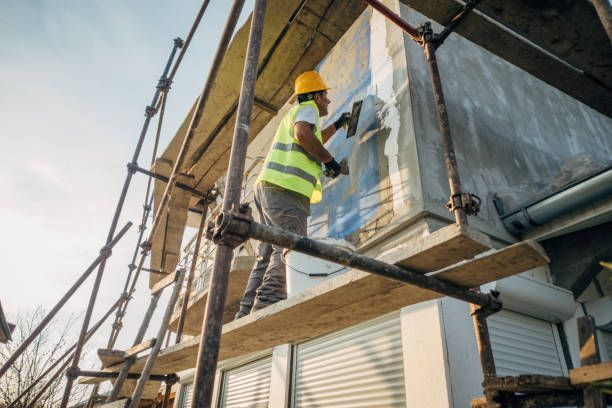 Construction worker on scaffolding applying stucco to a building exterior.