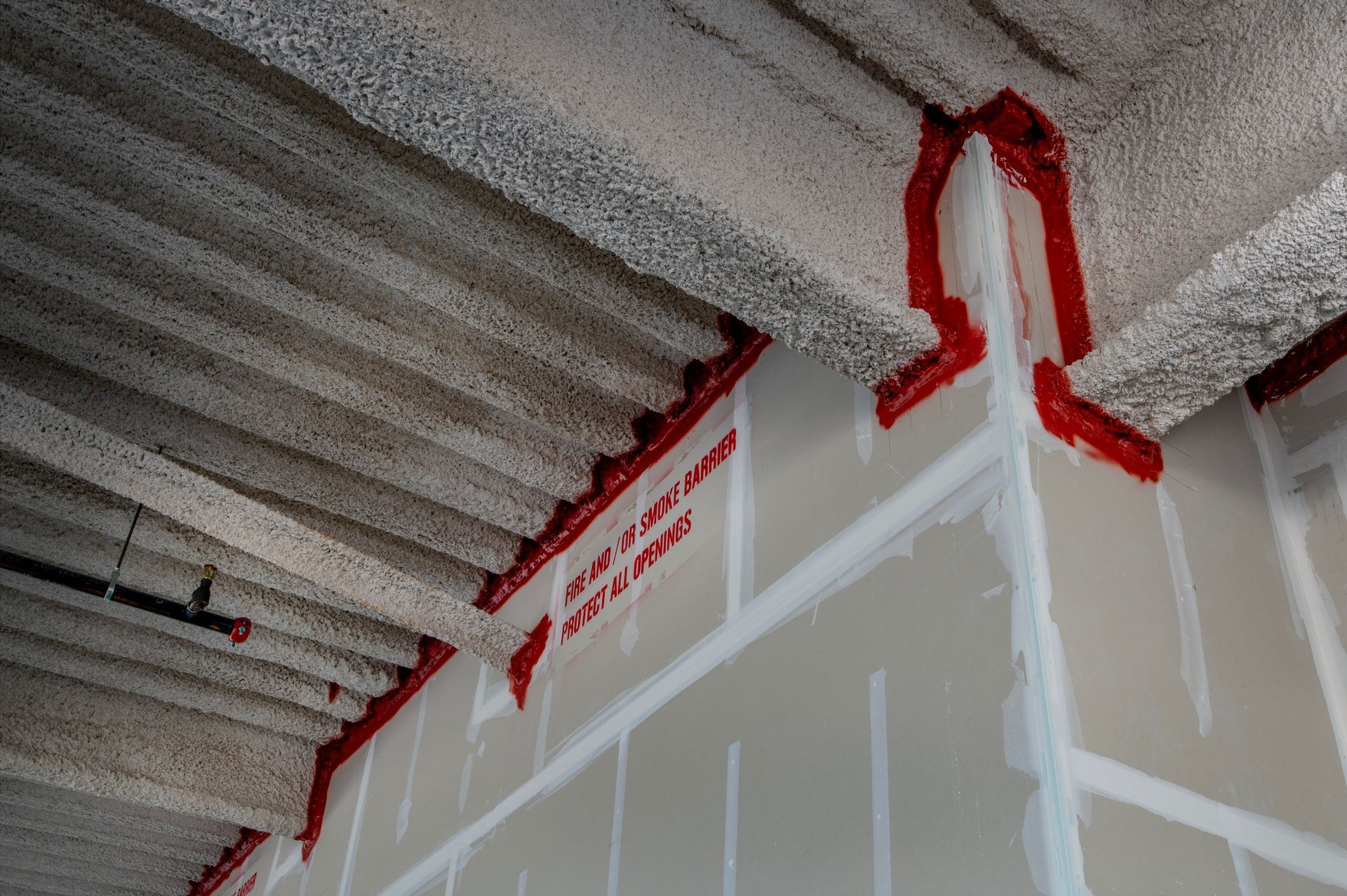 Red firestop sealant applied between drywall and ceiling deck.