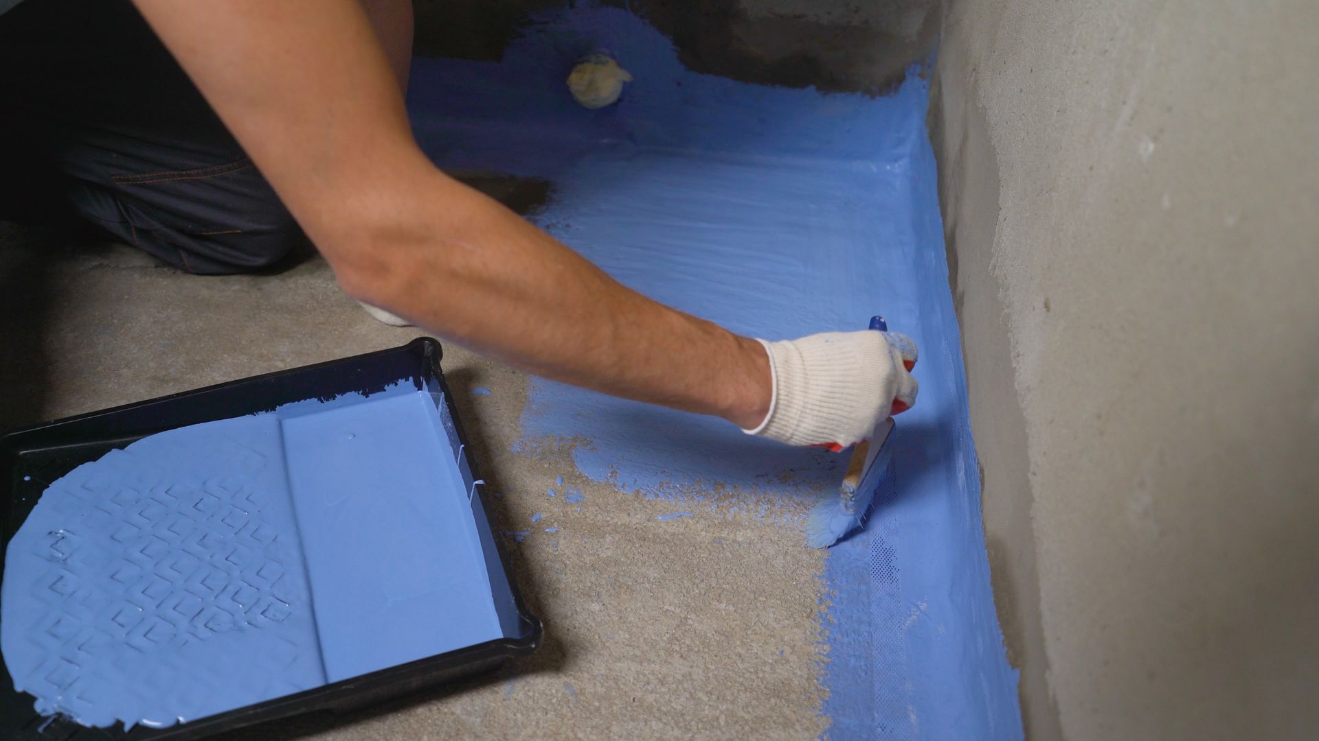 Person applying blue sealant to a shower floor with a brush and tray.