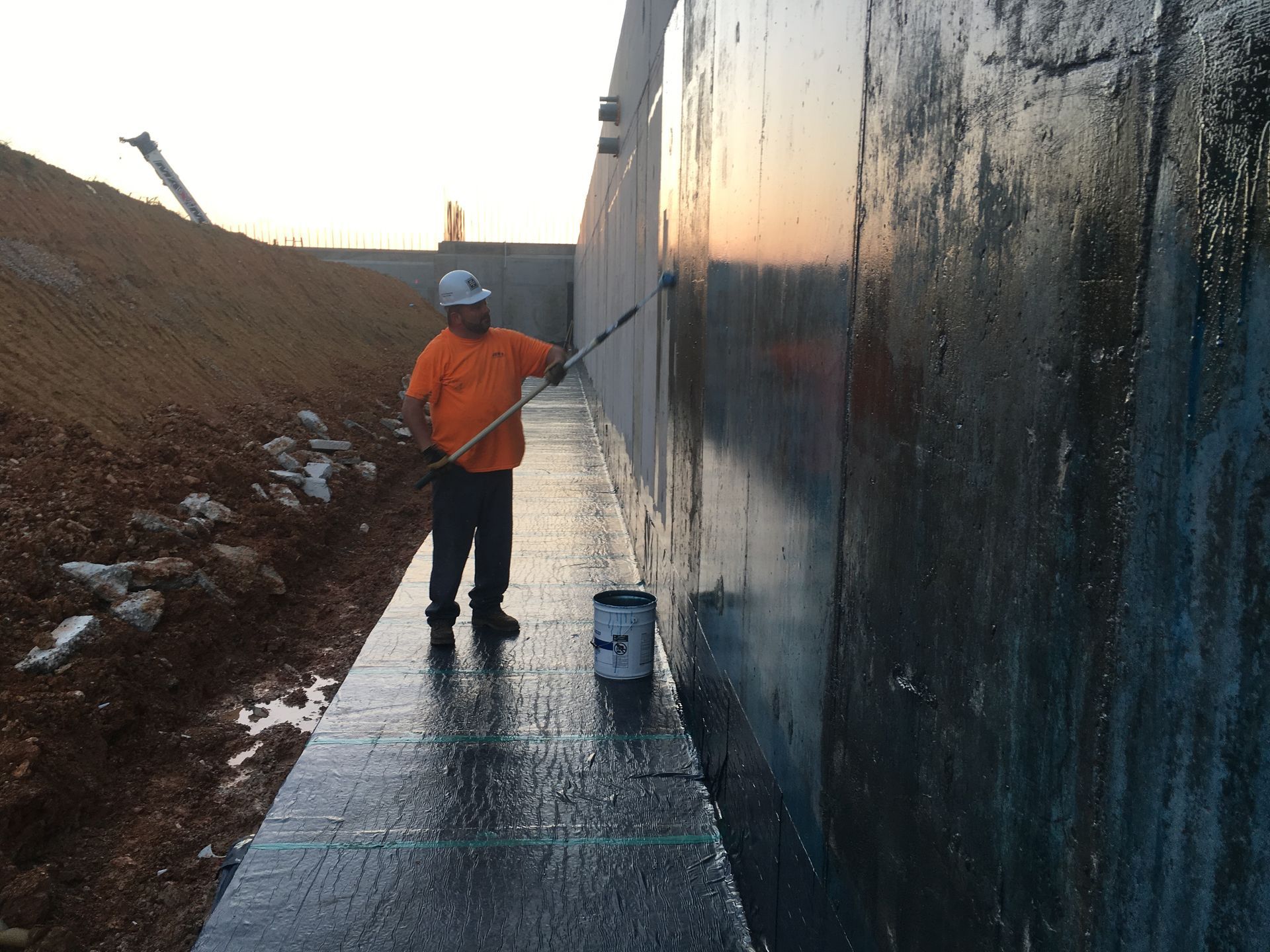 Three workers applying a dark sealant to a rooftop with brushes.