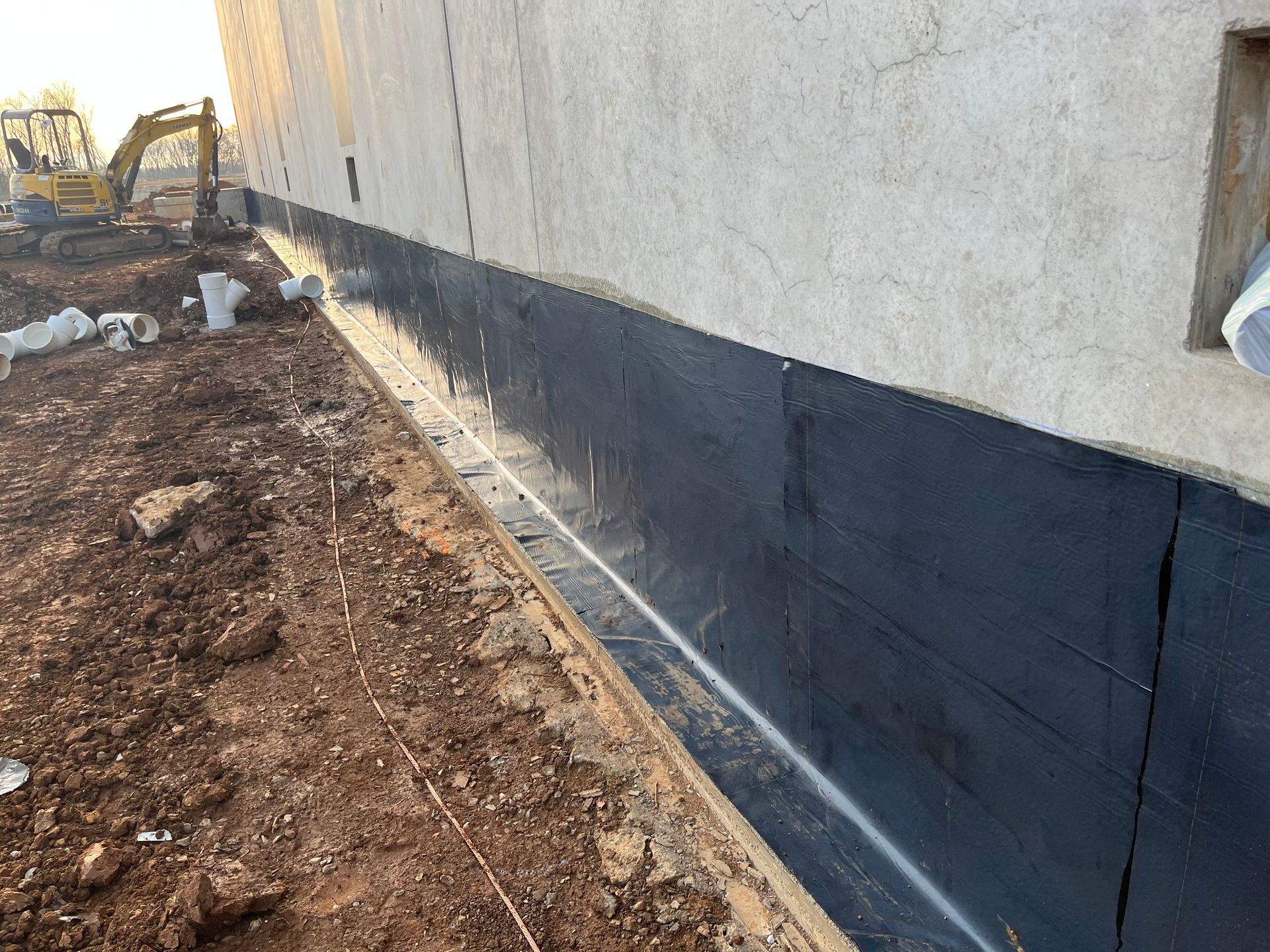 Person painting a floor with a roller, wearing work clothes and gloves. Light gray paint on the floor.