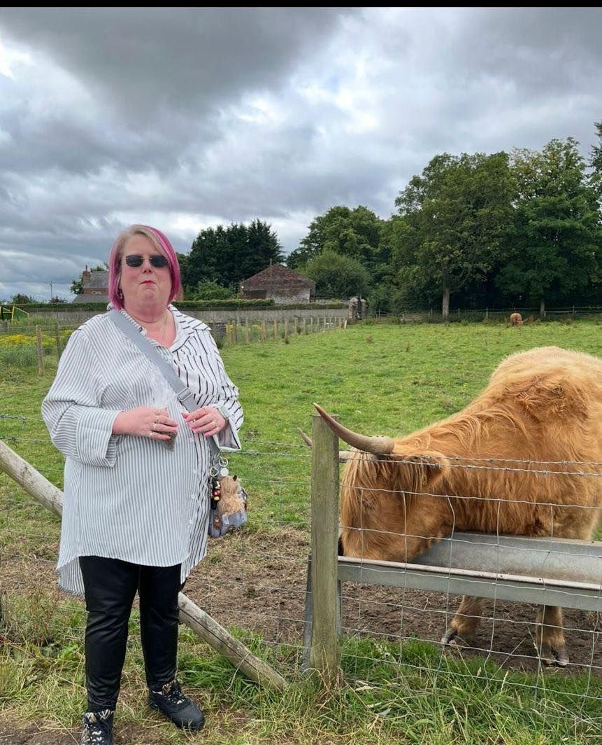 Woman standing next to a Highland cow in a grassy field on a cloudy day.