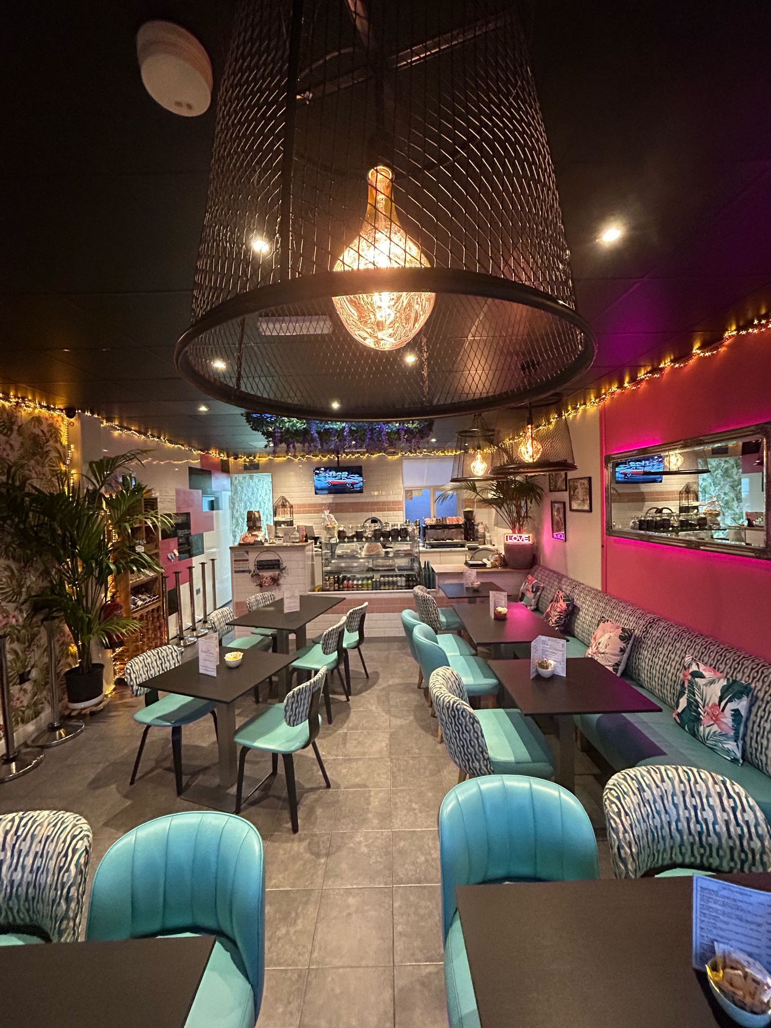 Restaurant interior with turquoise and pink decor, tables, and a large chandelier.