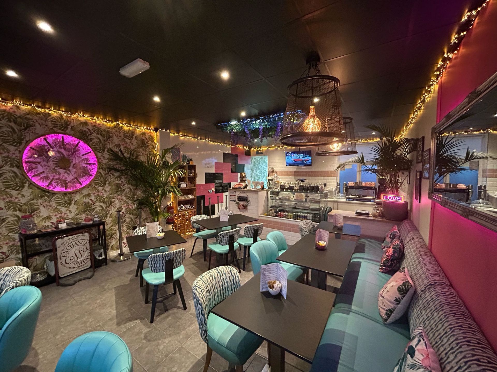 Cafe interior with tables, blue chairs, a pink wall, and decorative lighting.