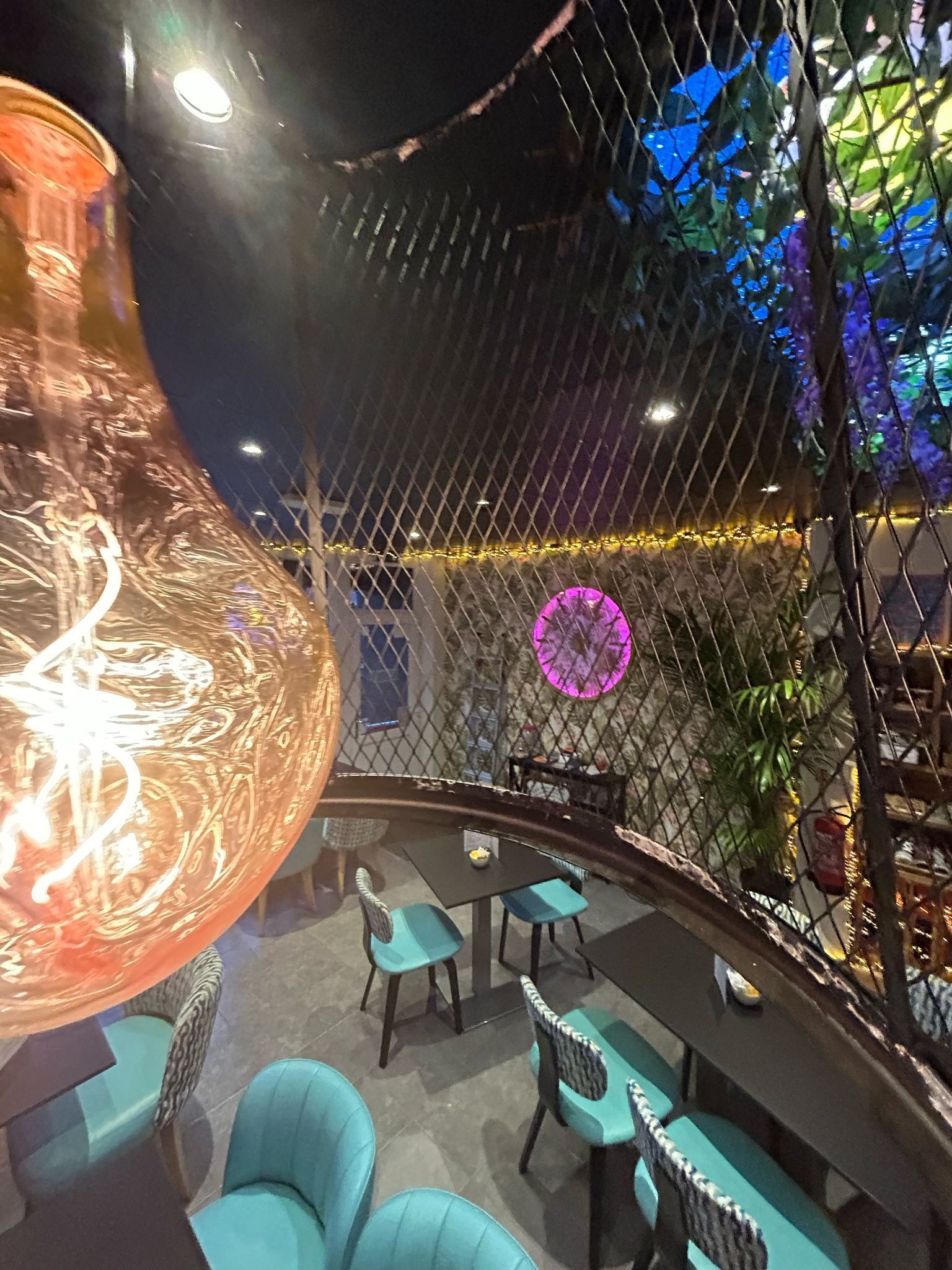 Restaurant interior with teal chairs, a round table, and a large decorative light fixture.