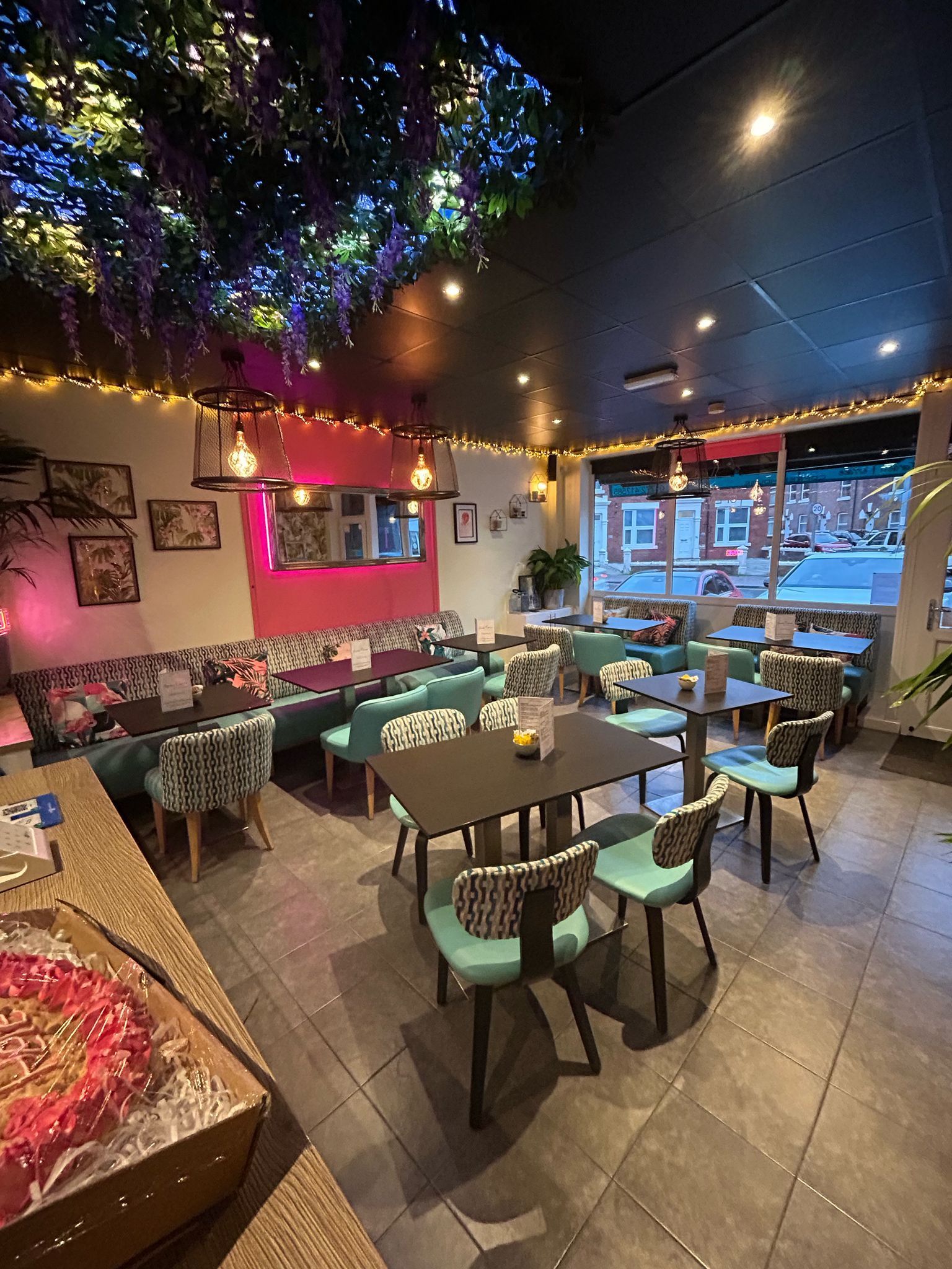 Interior of a cafe with teal seating, floral accents, and a pink wall, bathed in soft lighting.