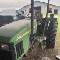 A green John Deere 5203 tractor parked on dirt outdoors with a pickup truck and barn in the background.