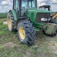 A green John Deere tractor parked on a grassy field under a cloudy sky.