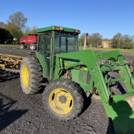 A green John Deere tractor with a front-end loader parked on a gravel lot under a clear blue sky.