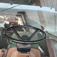 View from inside a tractor cab looking through the windshield at a shed and machinery.