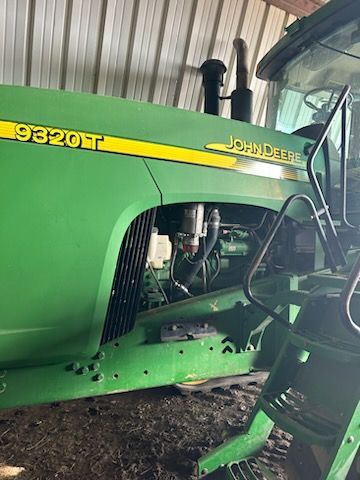 A green John Deere 9320T tractor showing the side of the engine compartment and access steps inside a shed.