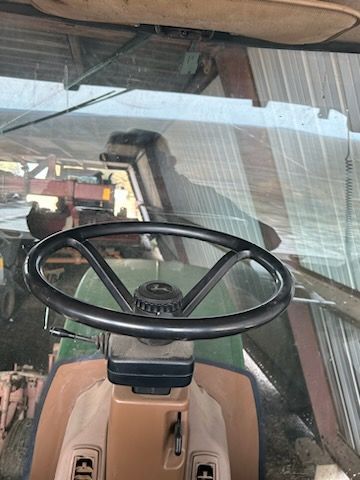 The view from the driver's seat of a John Deere tractor, showing the steering wheel and windshield inside a shed.