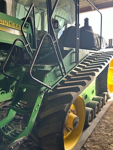 A close-up view of the green and yellow ladder and tracks of a large John Deere agricultural tractor inside a shed.