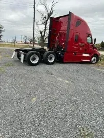 A red semi-truck tractor parked on a gravel lot under a cloudy sky.