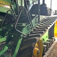 A close-up view of the black rubber tracks and yellow wheel of a green John Deere tractor with an access ladder.