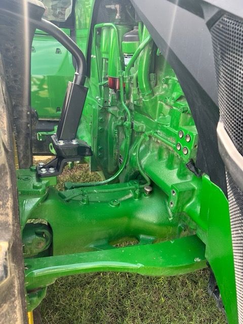 Close-up view of the bright green front axle, suspension, and hydraulic components of a John Deere tractor.