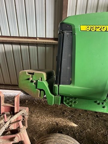 Close-up of the green hood of a John Deere 9320 tractor, showing its heavy front weight bracket in a storage shed.