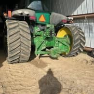 Rear view of a green John Deere tractor with large treaded tires parked on a dirt surface.