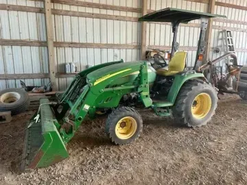 A green John Deere tractor with a front-end loader parked inside a wooden barn.
