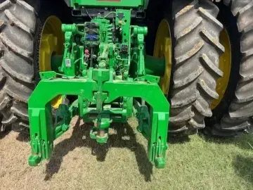 Rear view of a large John Deere tractor showing the green machinery of the rear hitch mechanism and deep-treaded tires.