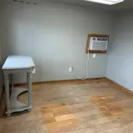 A gray wooden console table sits in the corner of a room with light gray walls and a wooden floor, next to a wall AC unit.
