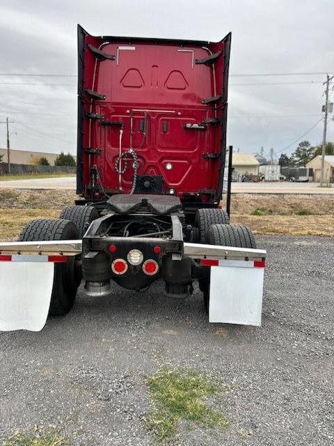 A red semi-truck cab, seen from the rear, parked on gravel with white mud flaps and exposed tires on a cloudy day.