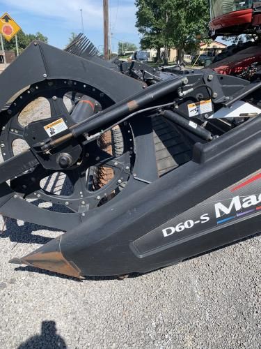 Close-up of a black MacDon D60-S combine draper header on a gravel lot under a bright, sunny sky.