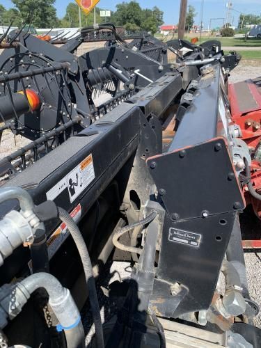 A close-up view of the black metal frame and hydraulic hoses of a combine harvester header sitting in an outdoor lot.