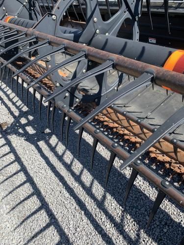Close-up view of the metal teeth and rotating reel assembly on an agricultural combine harvester header.