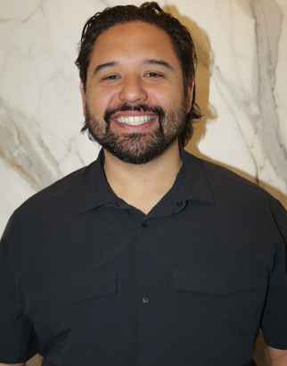 Smiling person in a black shirt standing in front of a light marble wall